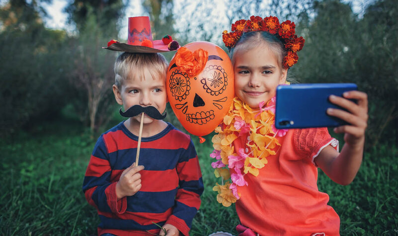 Day of the Dead and Halloween. Cute kids wearing in themed costumes for fun party Day of the Dead and Halloween. Cute kids wearing in themed costumes for fun party. Girl with orange flowers in her hair and boy with moustache in crafted Mexican sombrero, autumn lifestyle